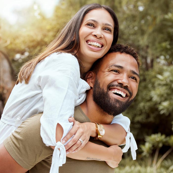 smiling man giving his wife a piggyback ride outside