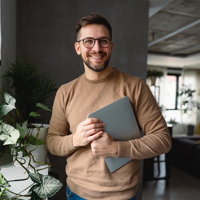 Young businessman smiling and holding a laptop in his modern apartment